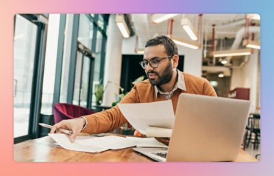 Seorang pria bekerja di depan komputer dengan kertas.