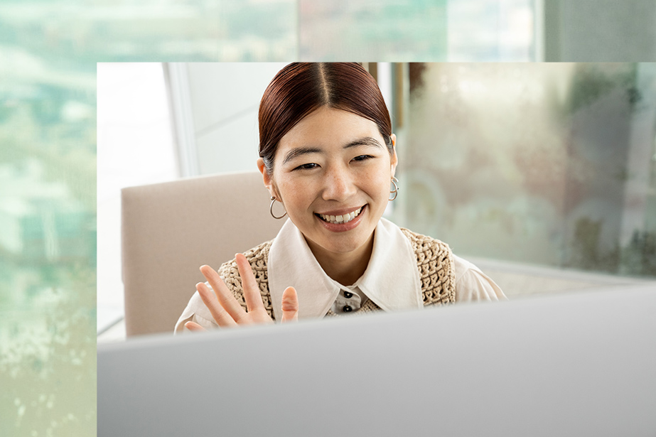 Une personne sourit et salue une personne devant un Surface Studio 2+.