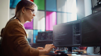 Een vrouw die voor een computerschermen zit.