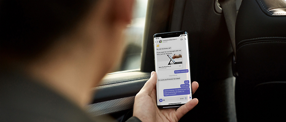 A person in a car looking at a smartphone displaying a messaging app with multiple conversations visible.