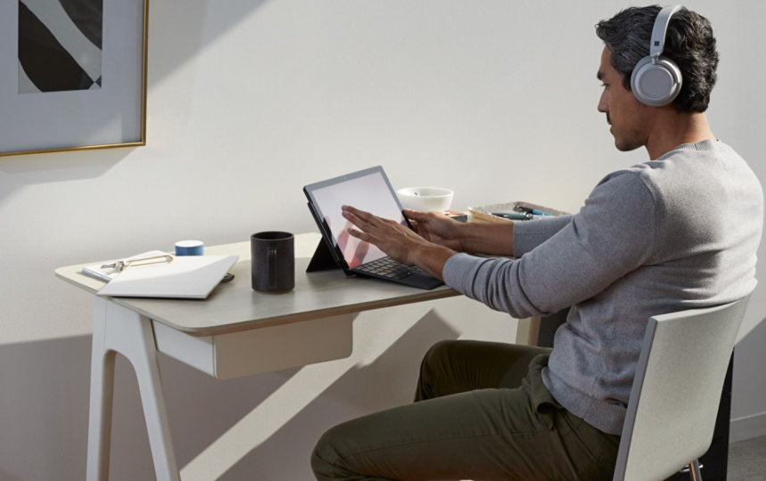 A person wearing headphones uses Surface Pro 7 at a desk at home.