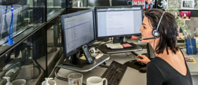 Predstavnica službe za korisnike koja nosi slušalice, radi za stolom sa više računarskih monitora.