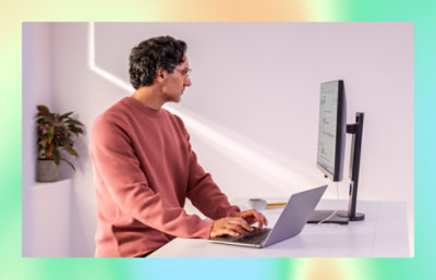 A man working typing in laptop and looking into desktop screen.