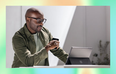 A man holding a mobile and looking into laptop screen.