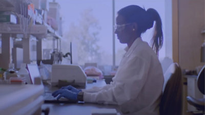 Une personne portant une blouse blanche et des gants travaillant sur un ordinateur.