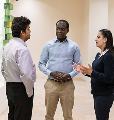 Three people standing and conversing in an indoor setting with faces obscured.