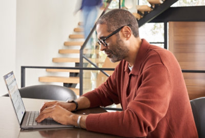 Person typing on a laptop while seated at a table in a modern workspace.