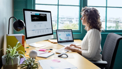 A woman sitting at a desk with a computer and a plant in the background.