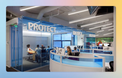 A group of people sitting at desks in a room with the word PROTECT visible.