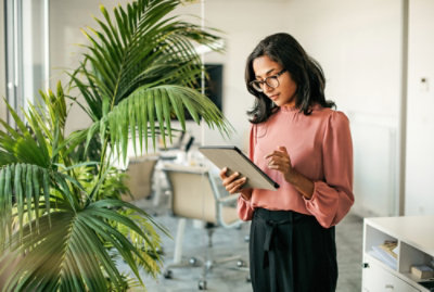 Person standing in an office, holding a tablet near indoor plants.