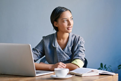 Person seated at a desk with a laptop, notebook, and coffee mug.