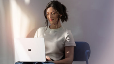 A person seated on a chair using a laptop in a softly lit indoor space with light-colored walls and natural sunlight casting shadows.