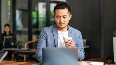 A person holding a cup and looking at a laptop.