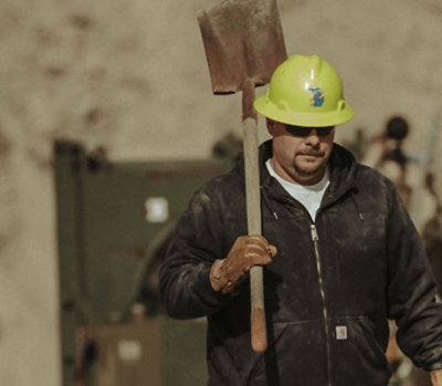A focused industrial worker wearing a safety helmet and carrying a shovel