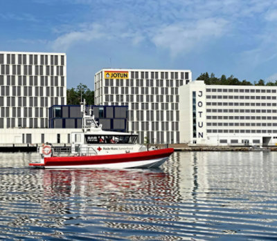 Office buildings along a waterfront with a boat passing in the foreground.