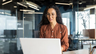 Person working on a laptop at a desk in a modern glass‑walled office.