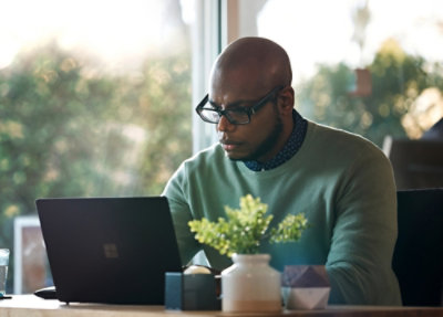 A man wearing glasses and looking down at a laptop.