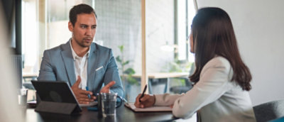 ผู้เชี่ยวชาญสองคนในการประชุม ผู้ชายกําลังพูดและแสดงท่าทาง ในขณะที่ผู้หญิงรับฟังและจดบันทึก