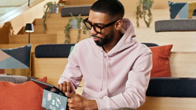 A man wearing glasses and a pink hoodie looking at a tablet.
