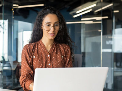 A woman with long hair wearing glasses working on a laptop with a white background and black text.