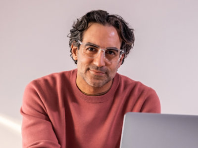 A man sitting at a desk with a laptop wearing glasses and a red shirt; green and black text on a white background reads: Save up to 76% versus pay-as-you-go pricing.