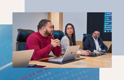 Grupa ljudi koji sede za stolom, uključujući osobu koja koristi laptop i druge koji nose raznovrsnu odeću.