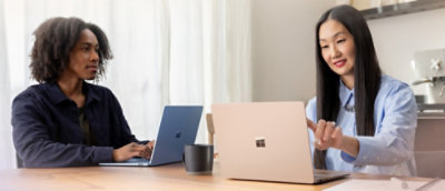 Two colleagues seated at a table, collaborating with laptops in a bright office setting.