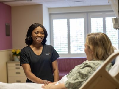 A Mercy nurse smiling while speaking with a patient at the bedside.