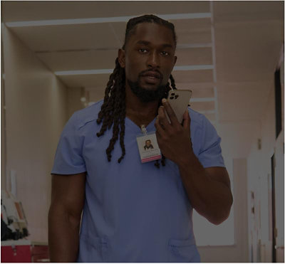 Healthcare worker in blue scrubs walking down a corridor while checking a mobile phone.