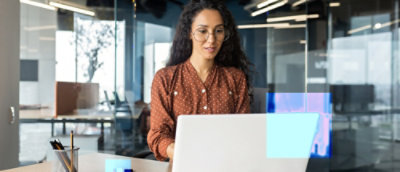A person wearing glasses looking at a laptop on a desk.