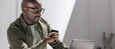 Person using a laptop while holding a smartphone at a desk.