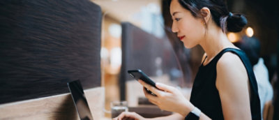 A person holding a phone and looking at a computer screen.