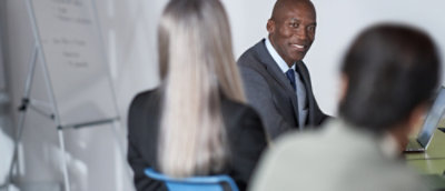 Small group meeting with participants seated around a table, reviewing content near a laptop and whiteboard.