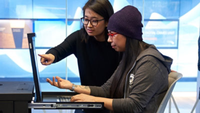 Two persons looking into laptop screen and takliking to each ohter.
