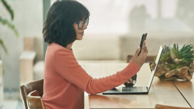 A woman holding a phone infront of her laptop