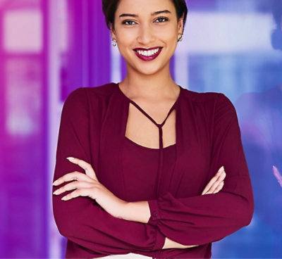 Person in a burgundy blouse with crisscross neckline standing with arms crossed against a blurred purple and blue background.