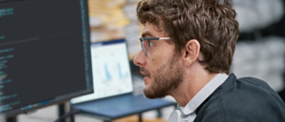A man with glasses and a beard looking at a computer screen.