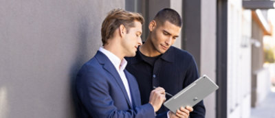 两位男士站着查看平板电脑。