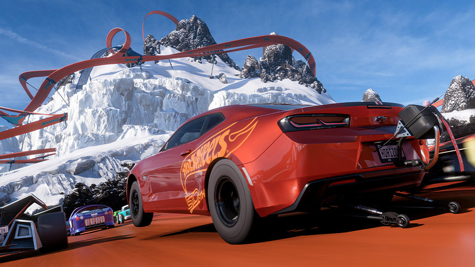 Forza Horizon 5. A Chevrolet Camaro with a Hot Wheels livery races down an orange track that wraps around the towering mountain ahead.