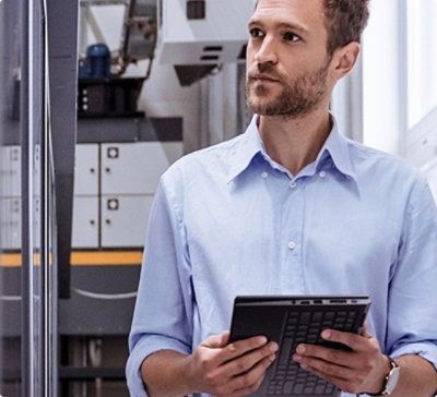 Person holding a tablet in an industrial or laboratory setting with machinery and equipment in the background.