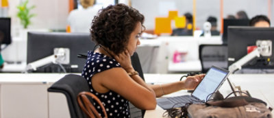 A woman with curly hair interacts with a computer screen, extending her hand towards it