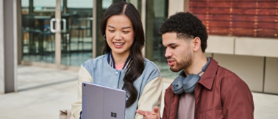 A man and woman are smiling together while looking at a laptop.