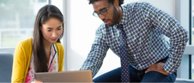 Két személy ülve nézi egy laptop képernyőjét egy irodai környezetben.