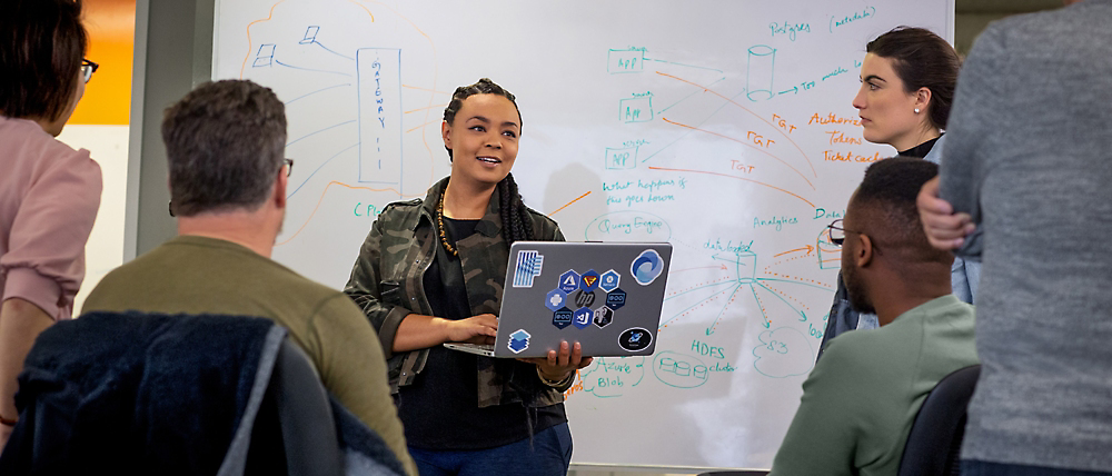 Uma mulher apresenta gráficos digitais num computador portátil a um grupo de colegas de trabalho atentos numa sala de conferências