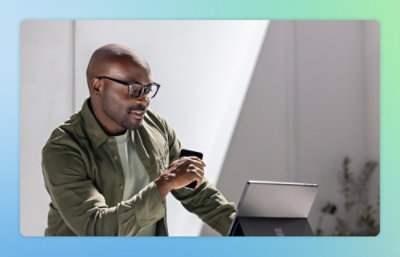 A man holding a phone and looking at a laptop.