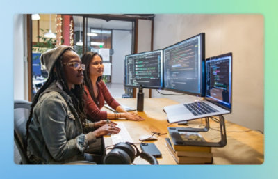 Two women sitting at a desk looking at a computer screen.