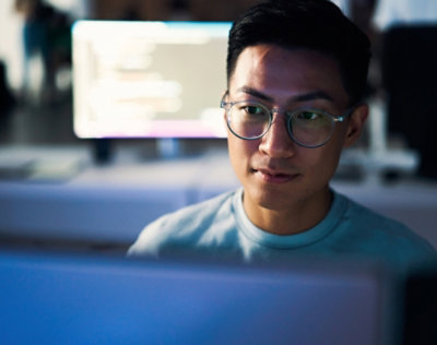  Person working at a computer with a monitor in a low‑light workspace.