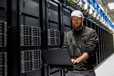 Person using a laptop beside server racks in a data center.