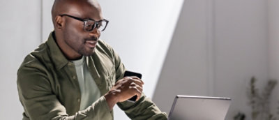 A man holding a coffee cup and looking at a laptop screen.