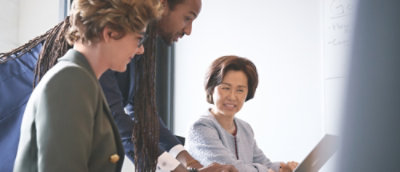 A man showing a laptop screen to two persons.